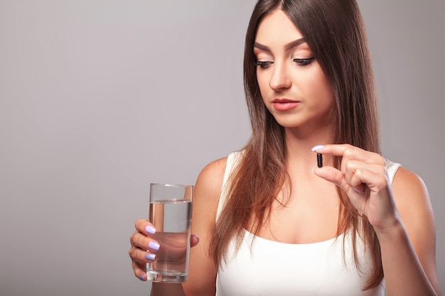 Resfriado y gripe. Mujer sosteniendo un vaso de agua y tomando cápsula