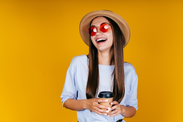 Un residente de verano se ríe con emoción de excelencia y mira a través de lentes rosas mientras sostiene un café. fondo amarillo