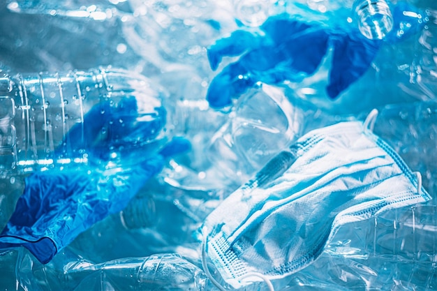 Residuos de covid19 Contaminación plástica Recogida de basura médica Guantes de mascarilla protectora azul descartados en desenfoque de fondo de textura de pila de botellas arrugadas usadas