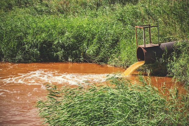 Resíduos industriais em forma de água laranja fluindo do cano para o rio