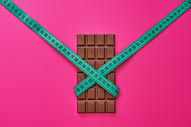 Resiste las tentaciones. Barra de chocolate envuelto con cinta métrica aislado sobre fondo de color rosa