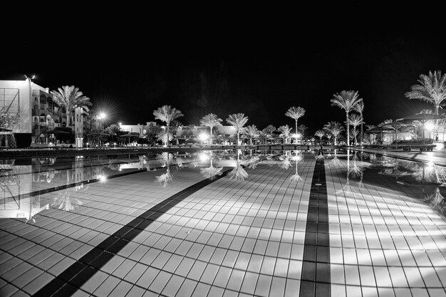 Resort de lujo piscina palmeras casas de hotel en idílica iluminación de luz nocturna y reflejo en la superficie de agua azul clara sobre fondo de cielo oscuro Bienestar y spa