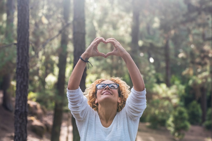 Foto respeite a natureza ao ar livre e salve o conceito do mundo da floresta com uma bela mulher adulta olhando para cima e fazendo o sinal de amor da lareira com as mãos
