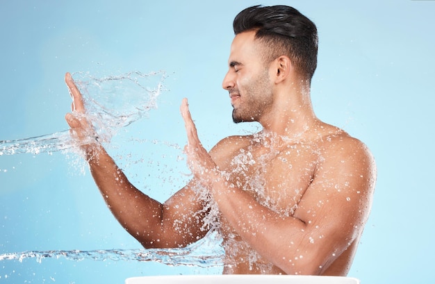 Foto respingos de água corporal e cuidados com a pele do homem limpando no estúdio isolado em um fundo azul gotas de água higiênica e modelo masculino lavando banho ou cuidando para pele saudável bem-estar facial ou beleza
