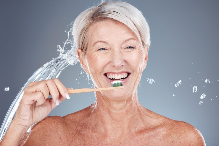Foto respingos de água de bem-estar e retrato de velha escovando os dentes isolados em fundo cinza no estúdio atendimento odontológico de bambu e limpeza de dentes feminina sênior com escova de dentes para higiene ecológica