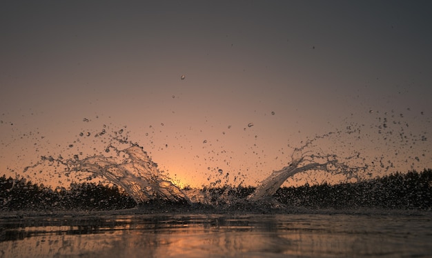 Respingos de água na superfície do lago. Céu do pôr do sol no fundo