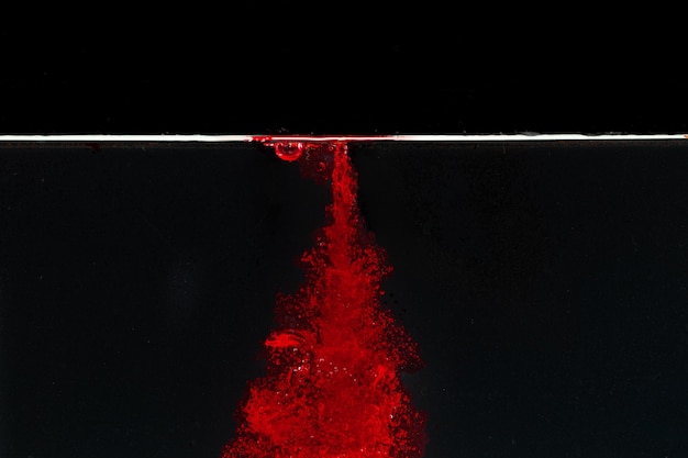 Respingos de água vermelha borbulhante em uma piscina contra um fundo preto