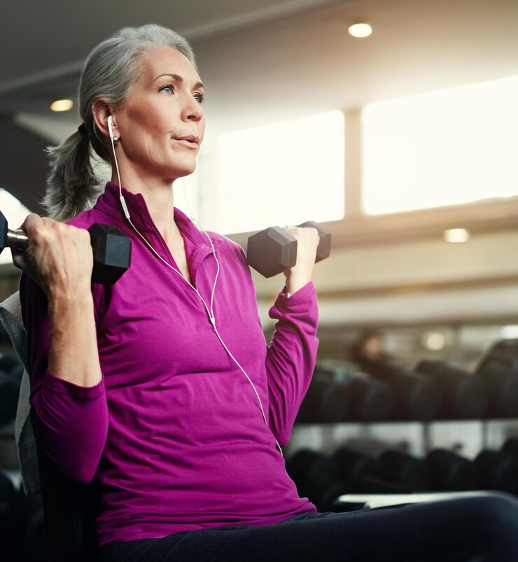 Foto respiração dumbbell e fitness com mulher madura em banco no ginásio para treinamento físico ou treino exercício saúde e música com atleta confiante pessoa em clube de desempenho para desafio ativo
