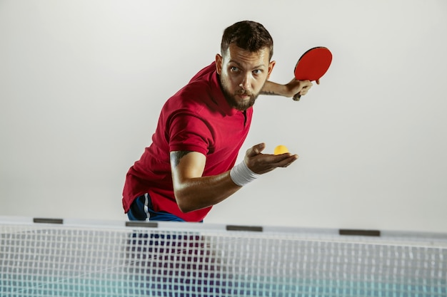 Respuesta. Joven juega tenis de mesa en la pared blanca. Modelo juega ping pong. Concepto de actividad de ocio, deporte, emociones humanas en el juego, estilo de vida saludable, movimiento, acción, movimiento.