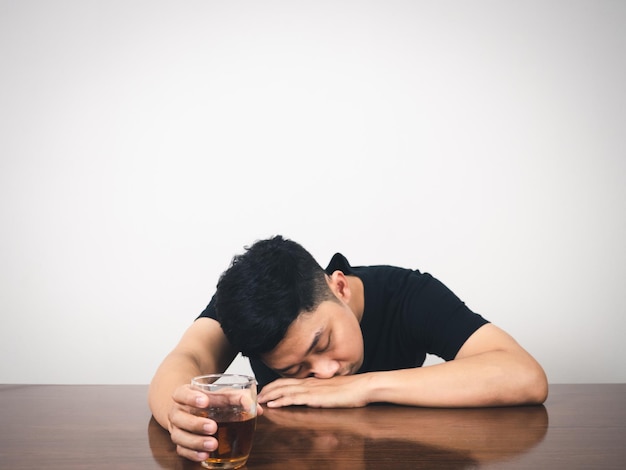 Ressaca do homem do alcoolismo deitado à mesa e segure o copo de álcool na mão