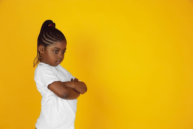 Ressentimento, rancor, tristeza. Retrato da menininha afro-americana em fundo amarelo studio. Garoto alegre e lindo. Conceito de emoções humanas, expressão, vendas, anúncio. Copyspace. Parece fofo.