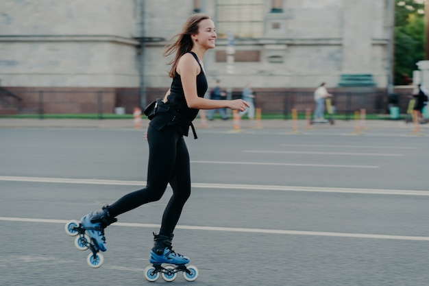 Rest Freizeit- und Lifestyle-Konzept. Fröhliche dunkelhaarige junge Europäerin atmet frische Luft, während Rollschuhlaufen ein Hobby hat, das einen aktiven Lebensstil führt und sich im Freien mit Fitnessaktivitäten beschäftigt