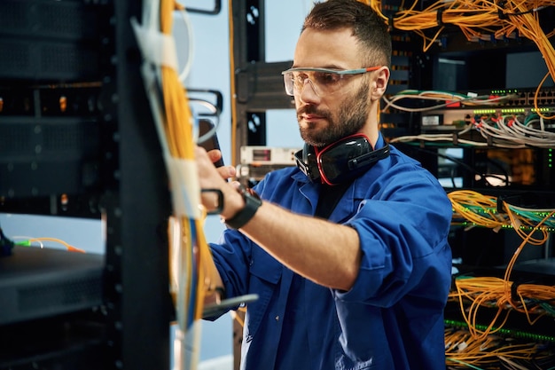 Restableciendo la conexión a Internet El joven está trabajando con equipos y cables en la sala de servidores