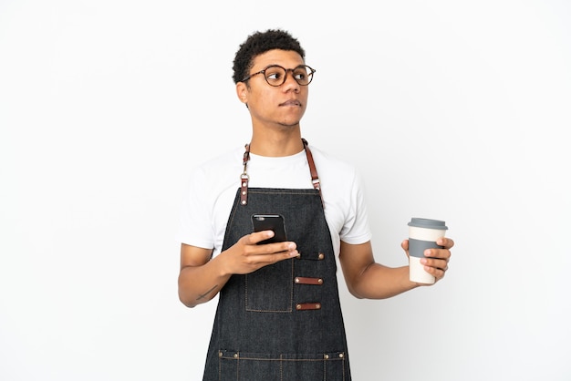 Restaurant African American Kellner Mann isoliert auf weißem Hintergrund hält Kaffee zum Mitnehmen und ein Handy, während er etwas denkt