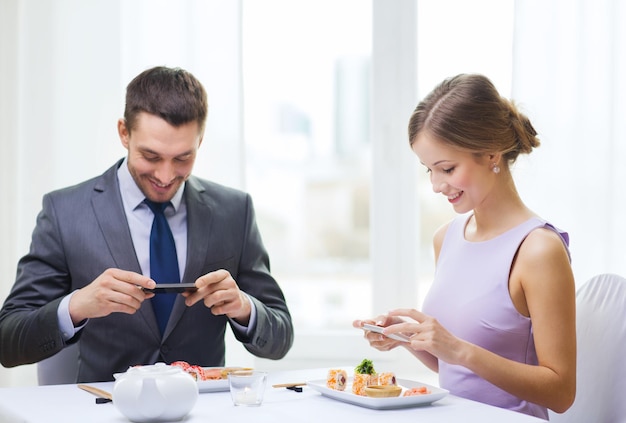 restaurant, paar, technologie und urlaubskonzept - lächelndes paar, das sushi mit smartphone-kamera im restaurant fotografiert