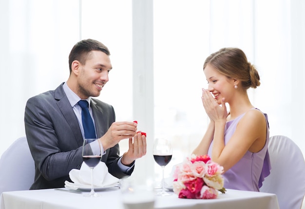 Restaurant-, Paar- und Urlaubskonzept - lächelnder Mann, der seiner Freundin im Restaurant einen Vorschlag macht