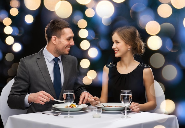 Restaurant-, Paar- und Urlaubskonzept - lächelndes Paar, das Hauptgericht im Restaurant isst