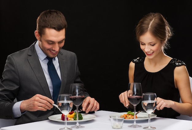 Restaurant-, Paar- und Urlaubskonzept - lächelndes Paar, das Hauptgericht mit Rotwein im Restaurant isst