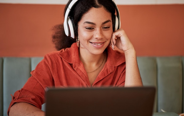 Restaurante de auriculares y mujer negra con una computadora portátil que transmite un video o podcast en la computadora. Estudiante que aprende en la web viendo o escuchando la radio de un joven feliz en una cafetería listo para estudiar.