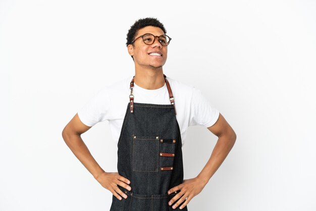 Restaurante camarero afroamericano hombre aislado sobre fondo blanco posando con los brazos en la cadera y sonriendo