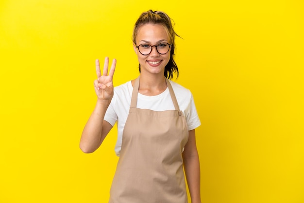 Restaurante camarero chica rusa aislada sobre fondo amarillo feliz y contando tres con los dedos