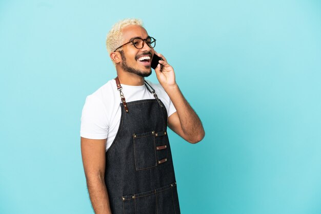 Restaurante camarero colombiano hombre aislado sobre fondo azul manteniendo una conversación con el teléfono móvil