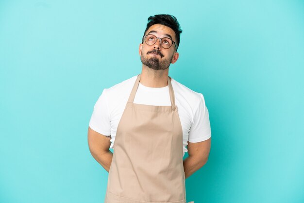 Restaurante camarero hombre caucásico aislado sobre fondo azul y mirando hacia arriba