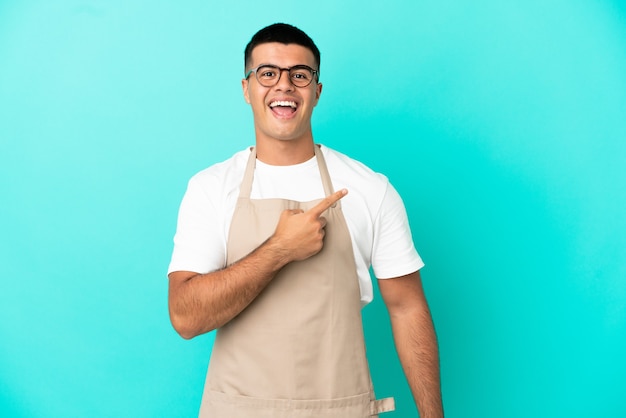 Restaurante camarero hombre sobre pared azul aislado sorprendido y apuntando hacia el lado