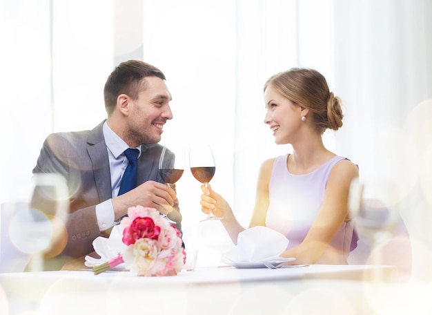 restaurante, casal e conceito de férias - casal jovem sorridente com copos de vinho tinto olhando uns aos outros no restaurante