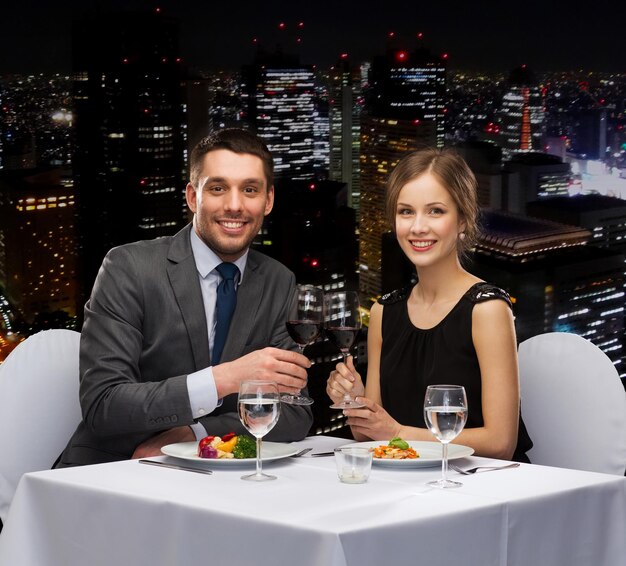 restaurante, casal e conceito de férias - casal sorridente comendo prato principal com vinho tinto no restaurante