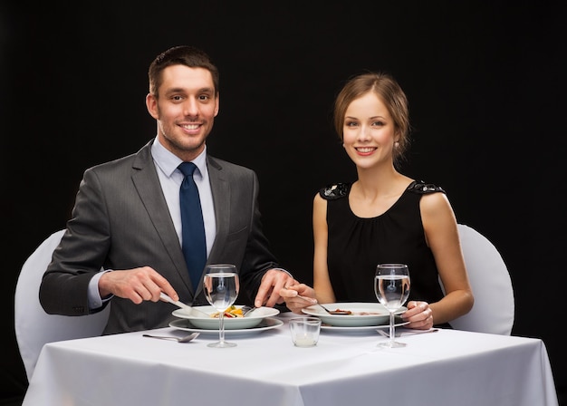 restaurante, casal e conceito de férias - casal sorridente comendo prato principal no restaurante