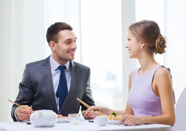 restaurante, casal e conceito de férias - casal sorridente comendo sushi no restaurante