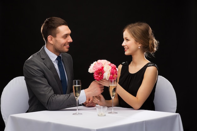 restaurante, casal e conceito de férias - homem sorridente dando buquê de flores para mulher no restaurante