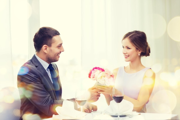 restaurante, casal e conceito de férias - homem sorridente dando namorada ou esposa buquê de flores no restaurante