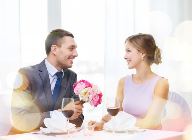 restaurante, casal e conceito de férias - homem sorridente dando namorada ou esposa buquê de flores no restaurante