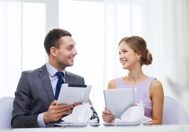 restaurante, casal, tecnologia e conceito de férias - casal sorridente com menus em computadores tablet pc no restaurante