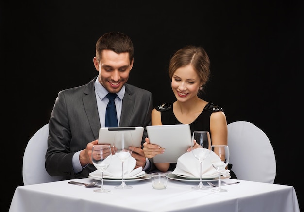 restaurante, casal, tecnologia e conceito de férias - casal sorridente com menus em computadores tablet pc no restaurante