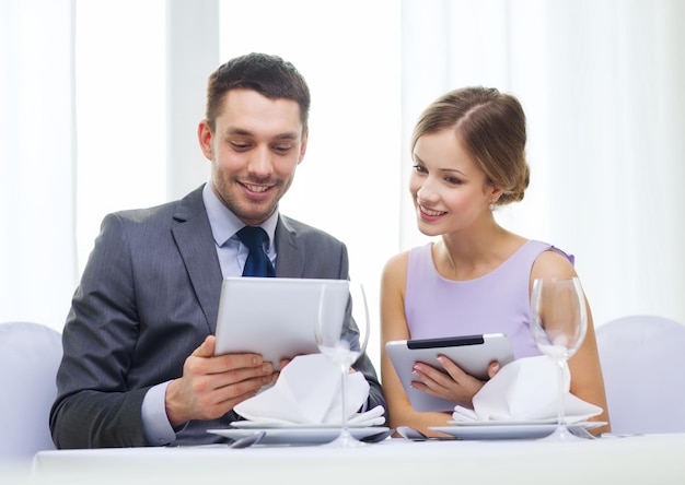 restaurante, casal, tecnologia e conceito de férias - jovem sorridente olhando para o menu de namorados ou maridos no computador tablet pc