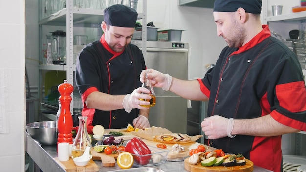 Restaurante cocina dos hombres trabajando en servir una ensalada con verduras fritas tomando un aceite