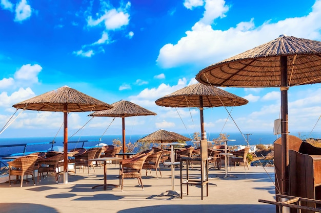 Restaurante com guarda-chuvas de palha na aldeia de oia, na ilha de santorini, mar egeu, grécia