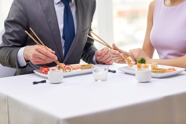 restaurante, comida, gente, fecha y concepto de vacaciones - cerca de una pareja comiendo sushi en el restaurante