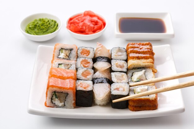 Restaurante de comida japonesa. Juego de sushi servido en bandeja blanca con salsa de soja, jengibre y wasabi y palillos escogiendo una pieza. Pov en fondo blanco