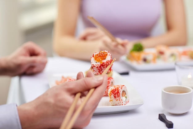 Restaurante, comida, pessoas, data e conceito de férias - close-up de casal comendo sushi no restaurante