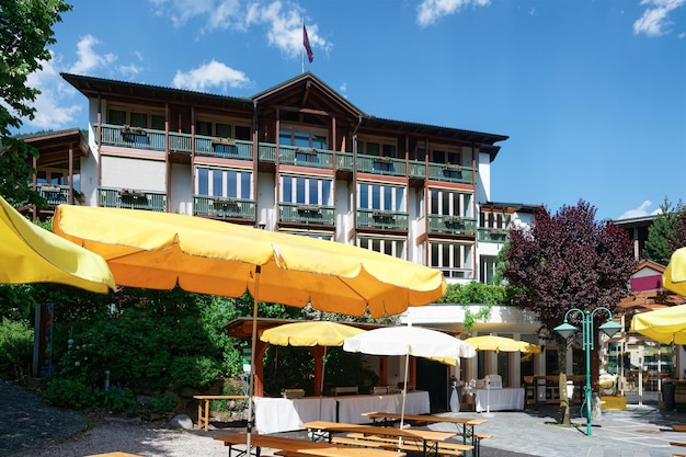 Restaurante de rua com guarda-sóis, mesas e cadeiras no hotel e resort familiar em Bad Kleinkirchheim na Caríntia, Áustria. Terraço do café da calçada e arquitetura do edifício com exterior. Estilo de vida