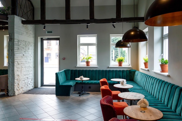 Un restaurante moderno y acogedor con sillas tapizadas de colores y cómodos sofás. Diseño de café inusual con paredes de hormigón en bruto y vigas decorativas de madera en el techo.