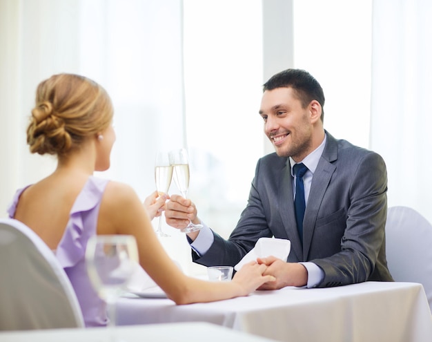 restaurante, pareja y concepto de vacaciones - hombre sonriente con una copa de champán mirando a su esposa o novia en el restaurante