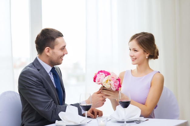 restaurante, pareja y concepto de vacaciones - hombre sonriente dando novia o esposa ramo de flores en el restaurante