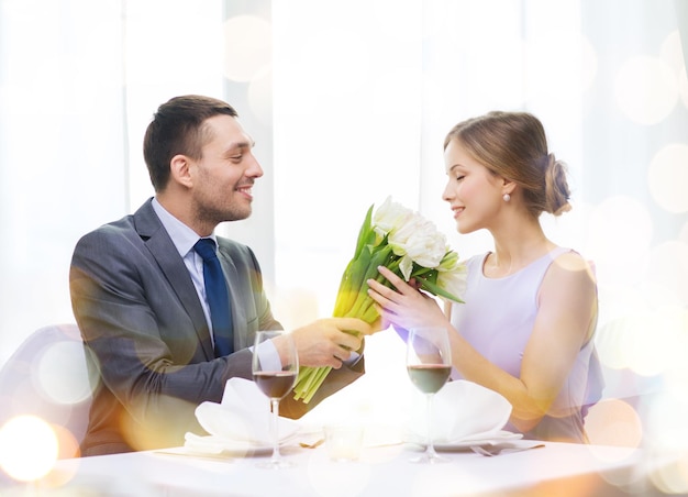 restaurante, pareja y concepto de vacaciones - hombre sonriente dando novia o esposa ramo de flores en el restaurante