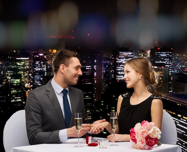 restaurante, pareja y concepto de vacaciones - hombre sonriente poniéndose un anillo de compromiso en el restaurante