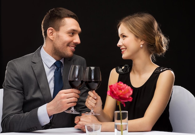 restaurante, pareja y concepto de vacaciones - pareja joven sonriente con copas de vino tinto mirándose en el restaurante